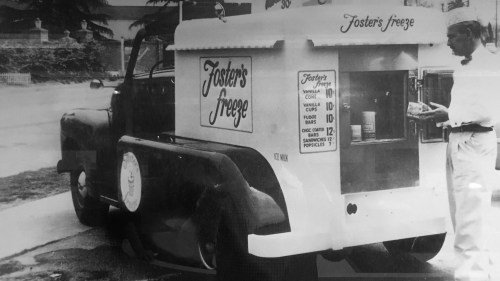 A vintage ice cream truck with "Foster's Freeze" signage, parked on a street while a man serves ice cream.