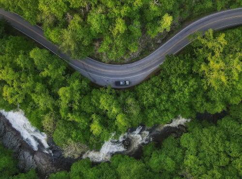 Aerial view of a winding road surrounded by lush green trees and a flowing river below.