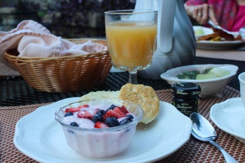 A breakfast table featuring yogurt with berries, a biscuit, a glass of juice, and a small jar of jam.