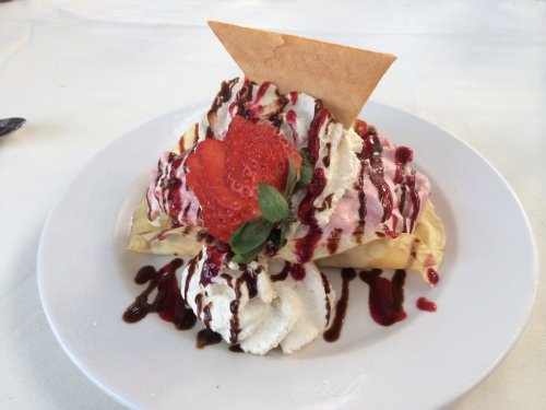A dessert plate featuring a waffle topped with whipped cream, strawberries, chocolate sauce, and a decorative cookie.