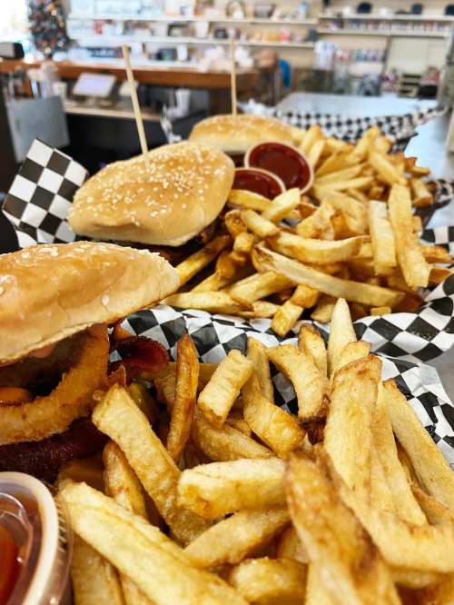 Two burgers with sesame seed buns and fries served in a basket, accompanied by dipping sauces.
