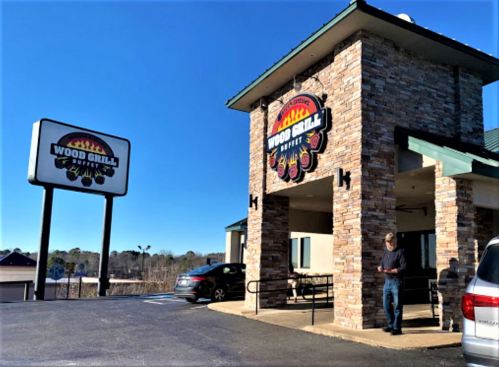 Exterior of Wood Grill restaurant with stone facade and a clear blue sky. A person stands near the entrance.
