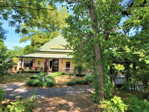 A charming yellow house with a green roof, surrounded by trees and greenery, featuring a welcoming porch.