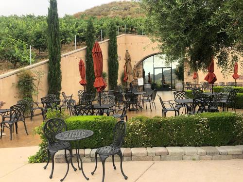 Outdoor seating area at a vineyard, featuring black metal tables, chairs, and red umbrellas surrounded by greenery.