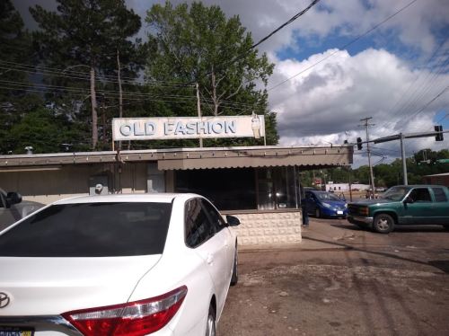 A white car parked in front of a diner with a sign reading "OLD FASHION" under a cloudy sky.