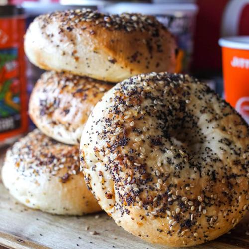 A stack of freshly baked bagels topped with sesame and poppy seeds on a wooden surface.