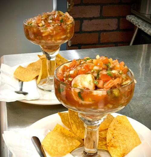 Two glasses of shrimp cocktail with diced tomatoes and herbs, served with tortilla chips on a plate.