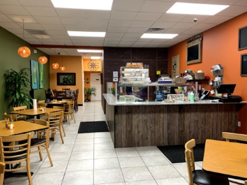 Cozy café interior with wooden tables, a counter displaying pastries, and colorful walls in green and orange.