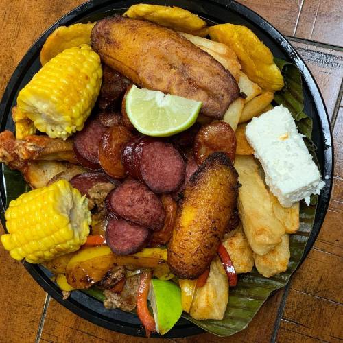 A colorful platter of fried plantains, corn, sausage, cheese, and fried vegetables, served on a banana leaf.