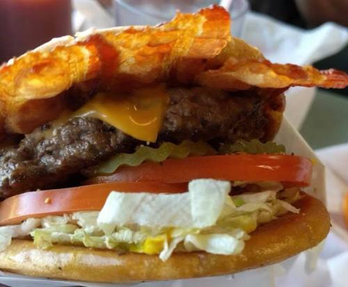 A close-up of a juicy hamburger with cheese, lettuce, tomato, pickles, and crispy bacon on a toasted bun.