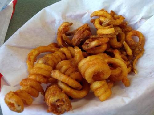 A serving of crispy, golden-brown curly fries on a white paper napkin.
