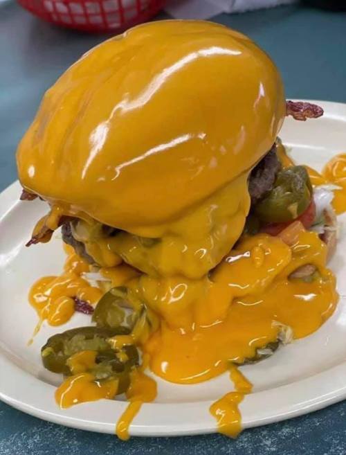 A towering cheeseburger topped with melted cheese, jalapeños, and bacon on a plate.