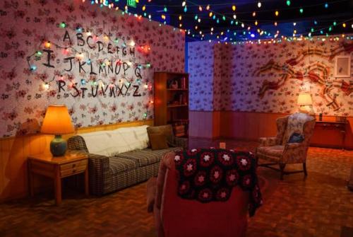 Cozy room with colorful string lights, floral wallpaper, a sofa, armchair, and a crocheted blanket.