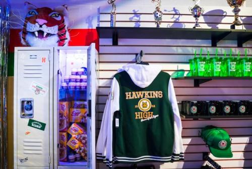 A green and white varsity jacket hangs next to a locker, trophies, and various merchandise in a themed display.
