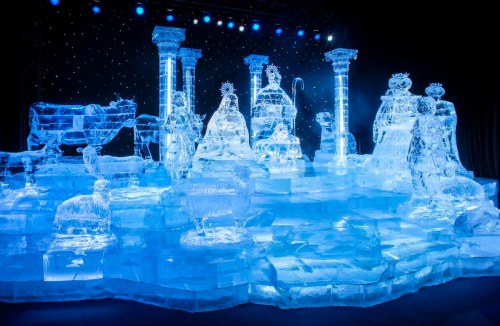 A stunning ice sculpture display featuring intricate figures and structures illuminated by blue lights.