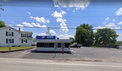A Dairy Queen restaurant with a drive-thru, set against a blue sky and a nearby house.