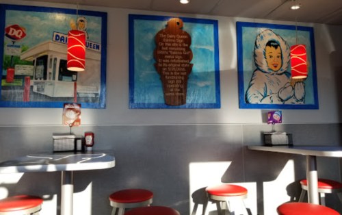 Interior of a Dairy Queen with colorful murals, red pendant lights, and empty tables and chairs.
