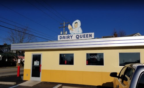 A Dairy Queen restaurant with a bright yellow exterior and a large ice cream cone sign on top against a clear blue sky.