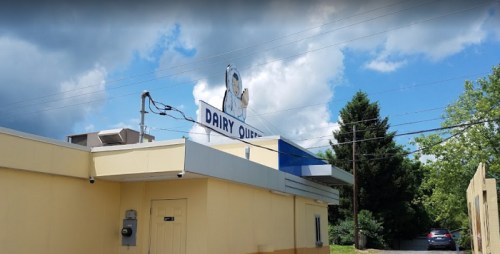 A Dairy Queen building with a blue and white sign under a partly cloudy sky, surrounded by trees and power lines.