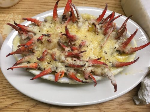 A dish featuring crab claws baked with cheese, arranged on a white plate.