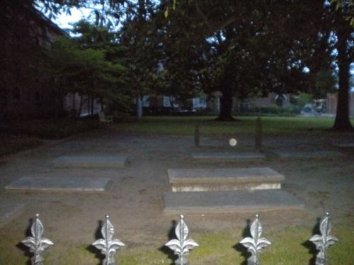 A dimly lit graveyard with several stone graves and a decorative metal fence in the foreground.