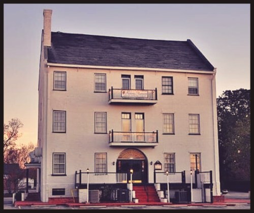 Historic white building with multiple balconies and a welcoming entrance, set against a soft sunset sky.