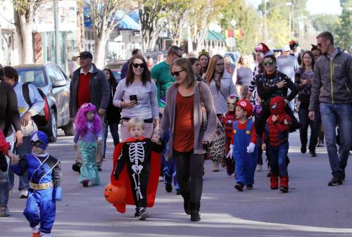 A lively street scene with families and children in costumes, celebrating a festive event.