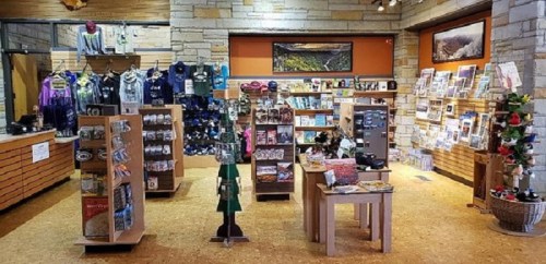 A cozy gift shop featuring shelves of merchandise, clothing, and local art in a warm, inviting space.