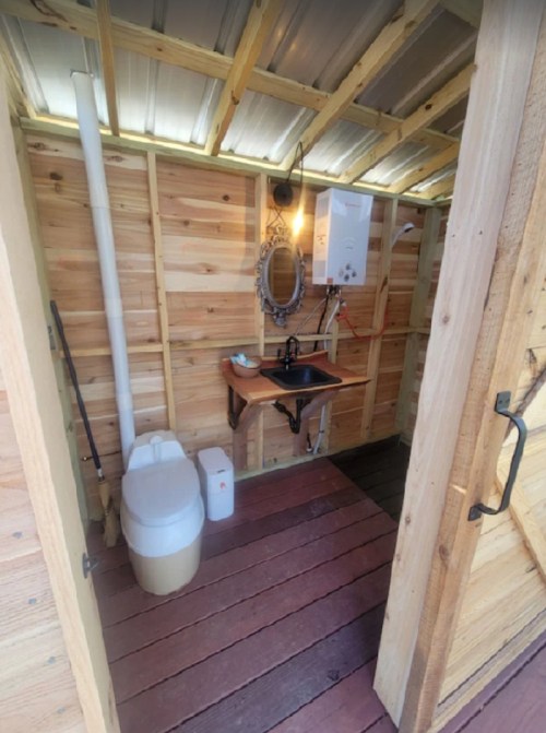 Interior of a small wooden bathroom featuring a toilet, sink, mirror, and wooden walls.