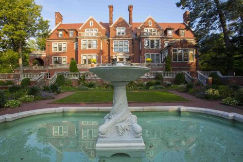 A grand brick mansion with multiple windows, surrounded by lush gardens and a decorative fountain in the foreground.