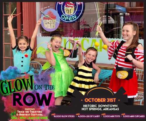 Four children in colorful costumes pose with glow sticks in front of a shop, promoting a Halloween festival in Hot Springs, Arkansas.