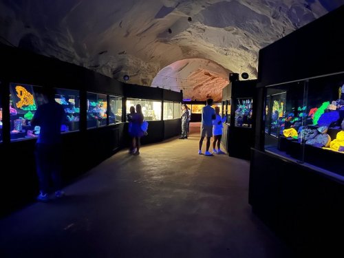 Visitors explore an underground aquarium, viewing brightly lit exhibits in a cavernous space.