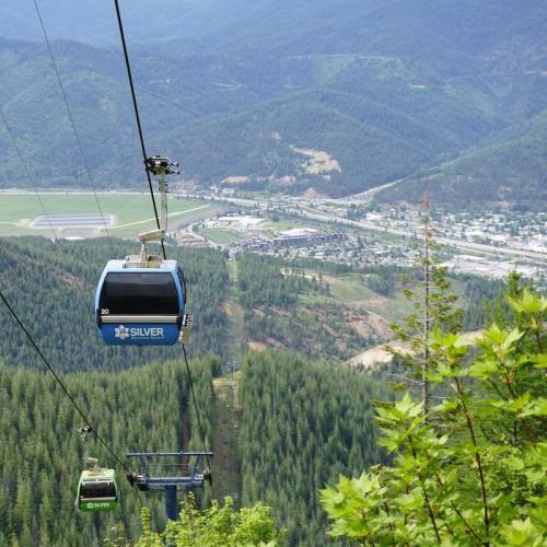 A scenic view of a cable car system above lush green mountains, with a valley and town visible in the background.