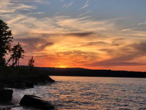 A vibrant sunset over a calm lake, with silhouettes of trees and rocky shoreline against a colorful sky.