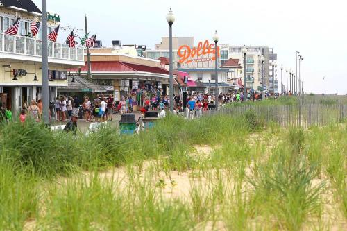 A busy boardwalk lined with shops and people, with tall grass in the foreground and a cloudy sky above.
