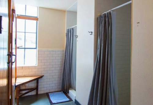 A clean, minimalist shower area with gray curtains, a bench, and large windows letting in natural light.