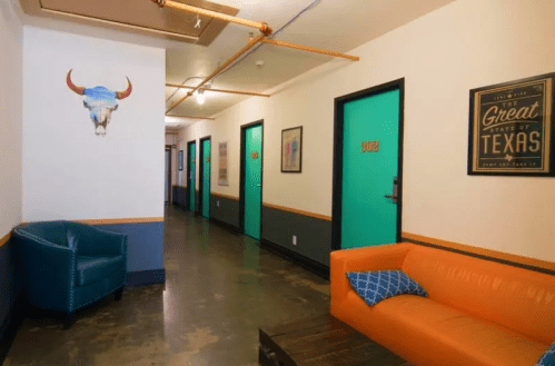 A hallway with teal doors, an orange couch, a blue chair, and a decorative bull skull on the wall.