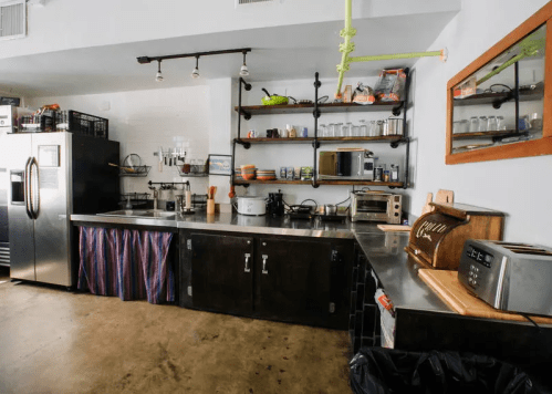 Modern kitchen with stainless steel counters, shelves, appliances, and a wooden breadbox.