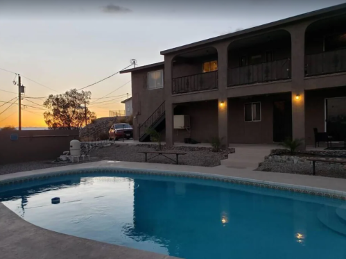 A tranquil backyard with a swimming pool, a two-story house, and a sunset in the background.