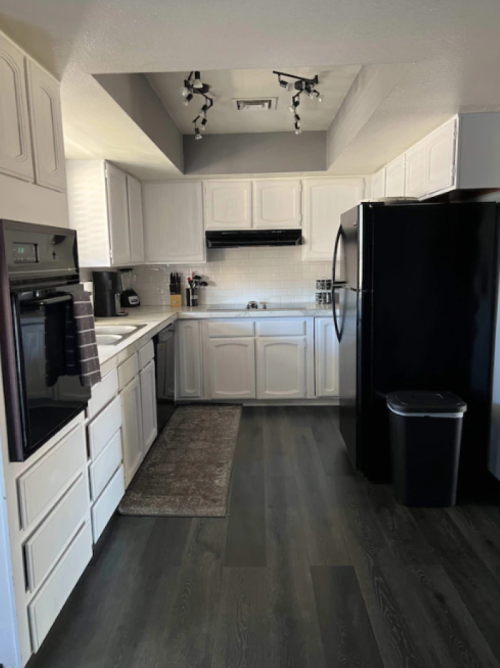 Modern kitchen with white cabinets, black appliances, and dark wood flooring. Bright and spacious layout.