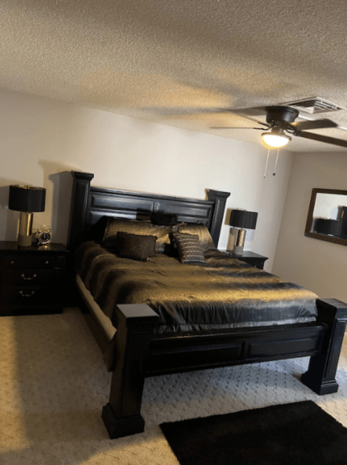A stylish bedroom featuring a black bed, matching nightstands, lamps, and a large mirror on the wall.