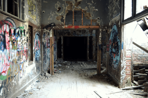 A dimly lit, abandoned hallway with graffiti-covered walls and debris scattered on the floor.