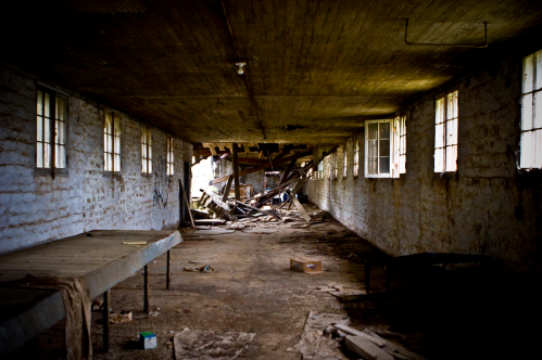 An abandoned, dilapidated room with broken windows, debris, and a dusty floor, evoking a sense of neglect.