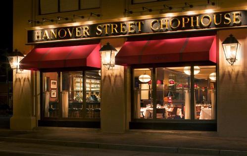 Exterior of Hanover Street Chophouse at night, featuring warm lighting and elegant dining setup visible through large windows.