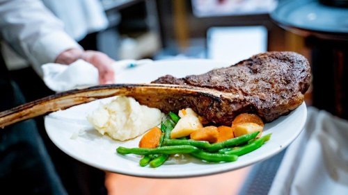 A large ribeye steak on a plate with mashed potatoes and mixed vegetables, served by a waiter.