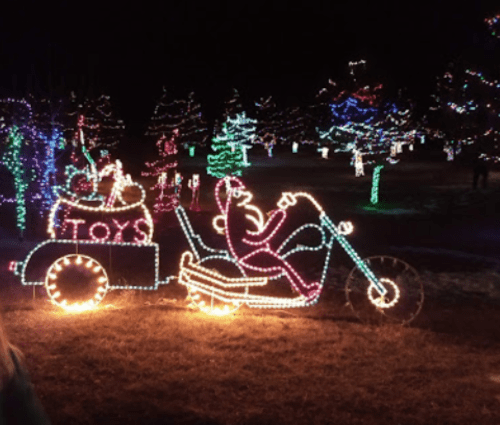 Colorful holiday lights depict a motorcycle with a Santa figure and a trailer labeled "TOYS" in a festive nighttime setting.