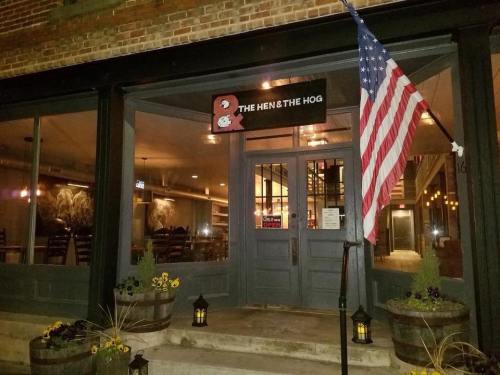 Exterior view of "The Hen & The Hog" restaurant at night, featuring an American flag and decorative plants.