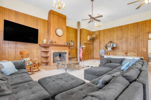 Cozy living room with wooden walls, a fireplace, large sectional sofa, and decorative elements like a clock and chandelier.