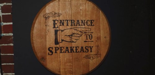 Wooden sign with vintage design, reading "Entrance to Speakeasy," featuring a pointing hand illustration.