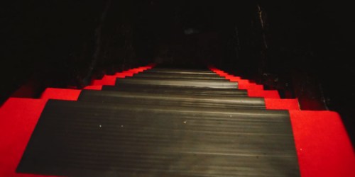 A dark staircase with black steps and bright red edges, leading down into a shadowy space.
